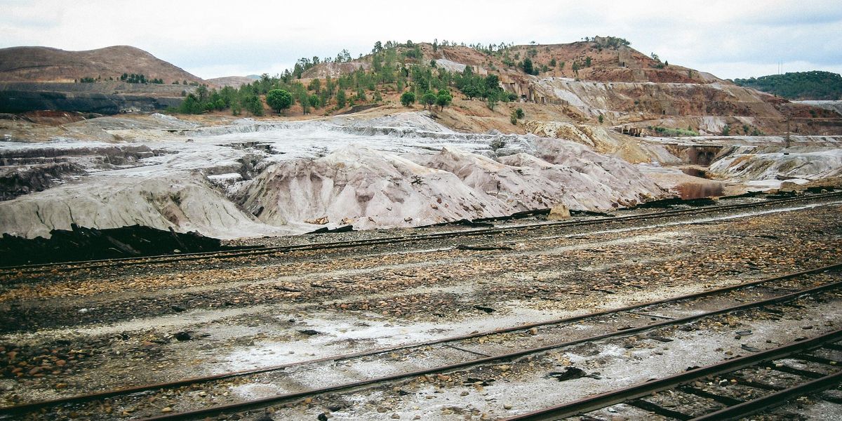A train track with a mountain and piles of soil waste in the background.