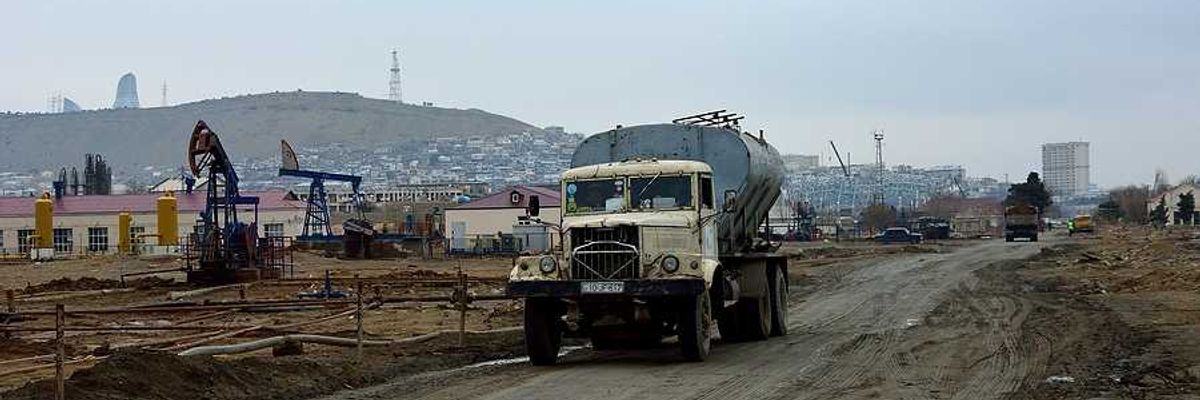 A truck drives down a muddy road next to aging oil pumps
