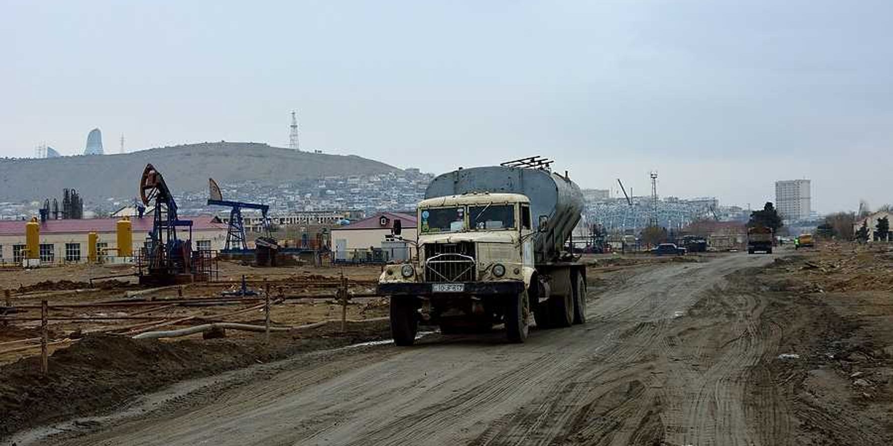 A truck drives down a muddy road next to aging oil pumps