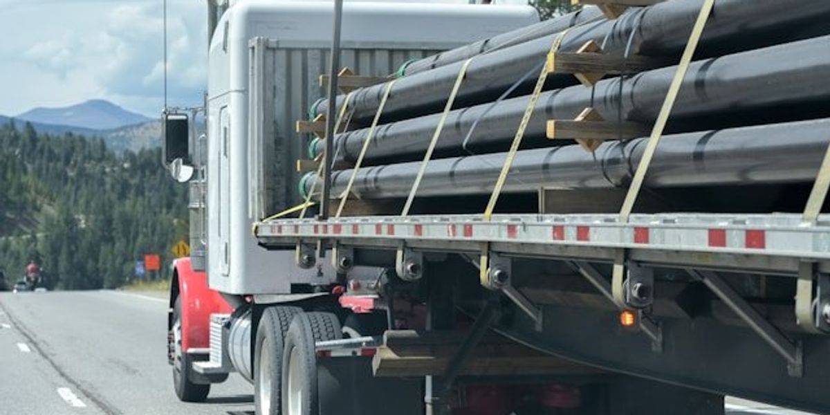 A truck with rows of pipeline tied to the flatbed.