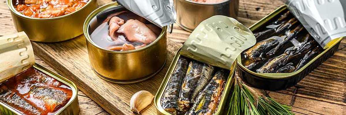 A variety of canned fish in metal cans with the lids open on a wood surface