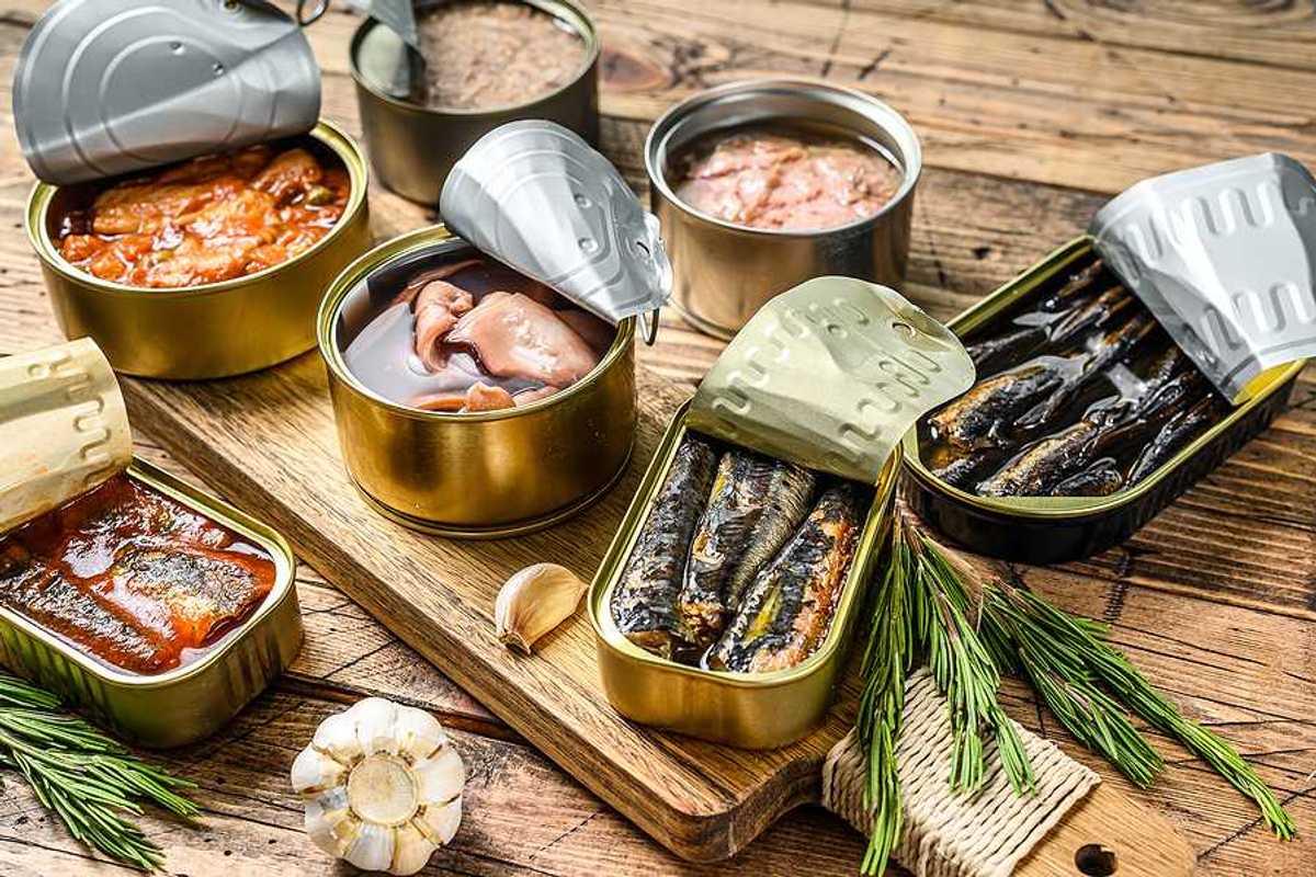 A variety of canned fish in metal cans with the lids open on a wood surface