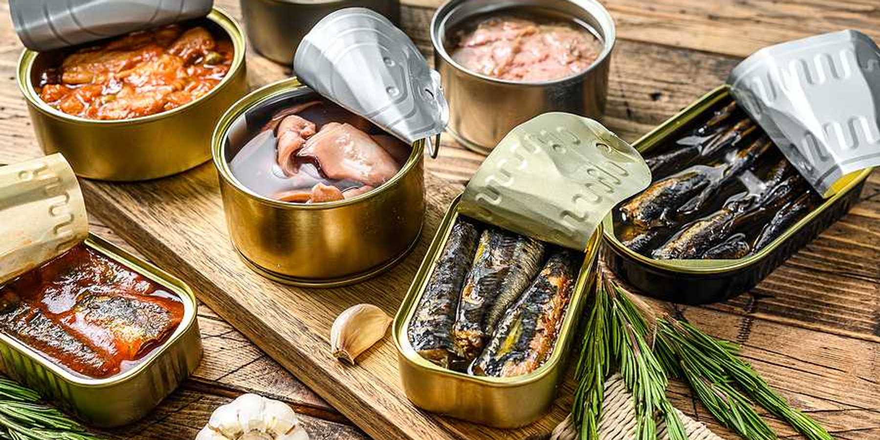 A variety of canned fish in metal cans with the lids open on a wood surface