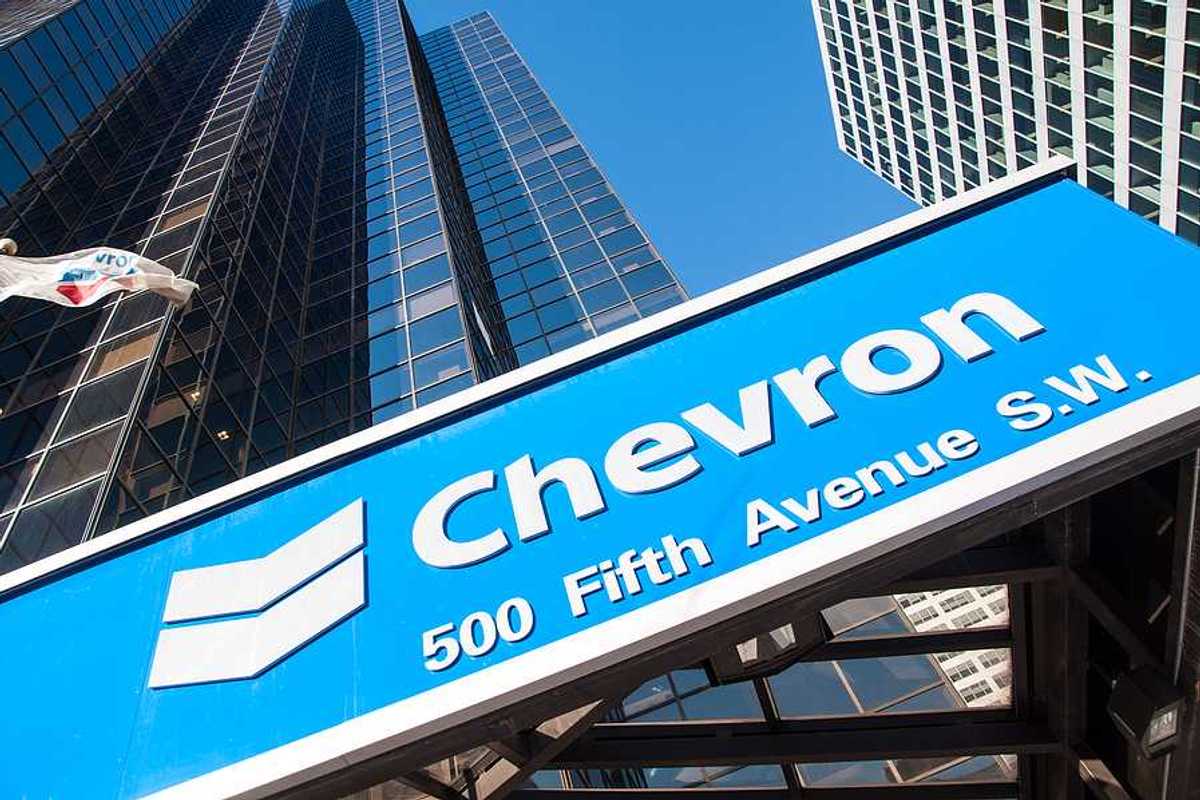 A view of a blue Chevron sign with rising sky scrapers behind it