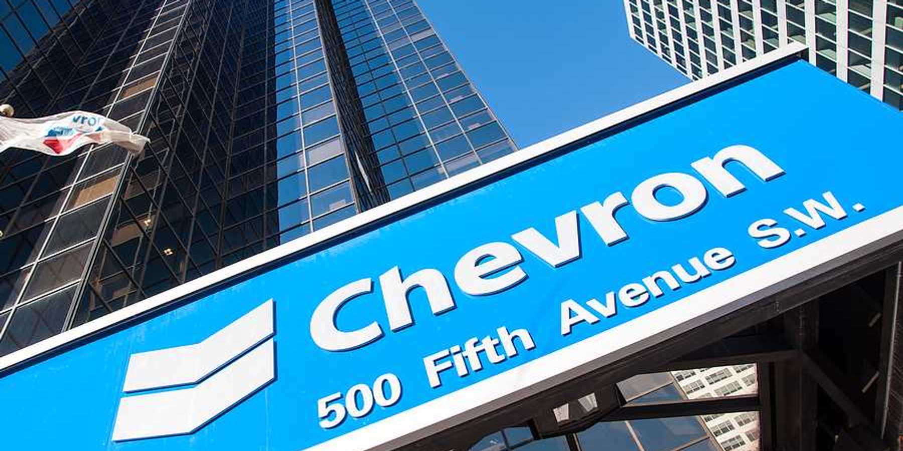 A view of a blue Chevron sign with rising sky scrapers behind it