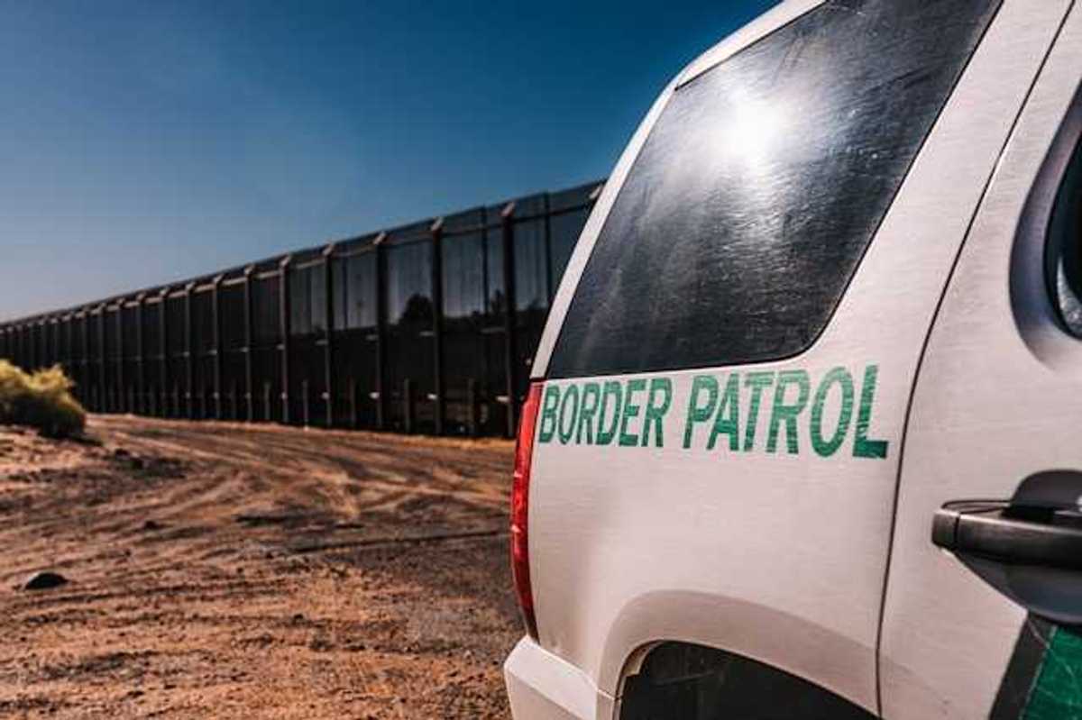 A view of a Border Patrol vehicle next to a tall metal border wall