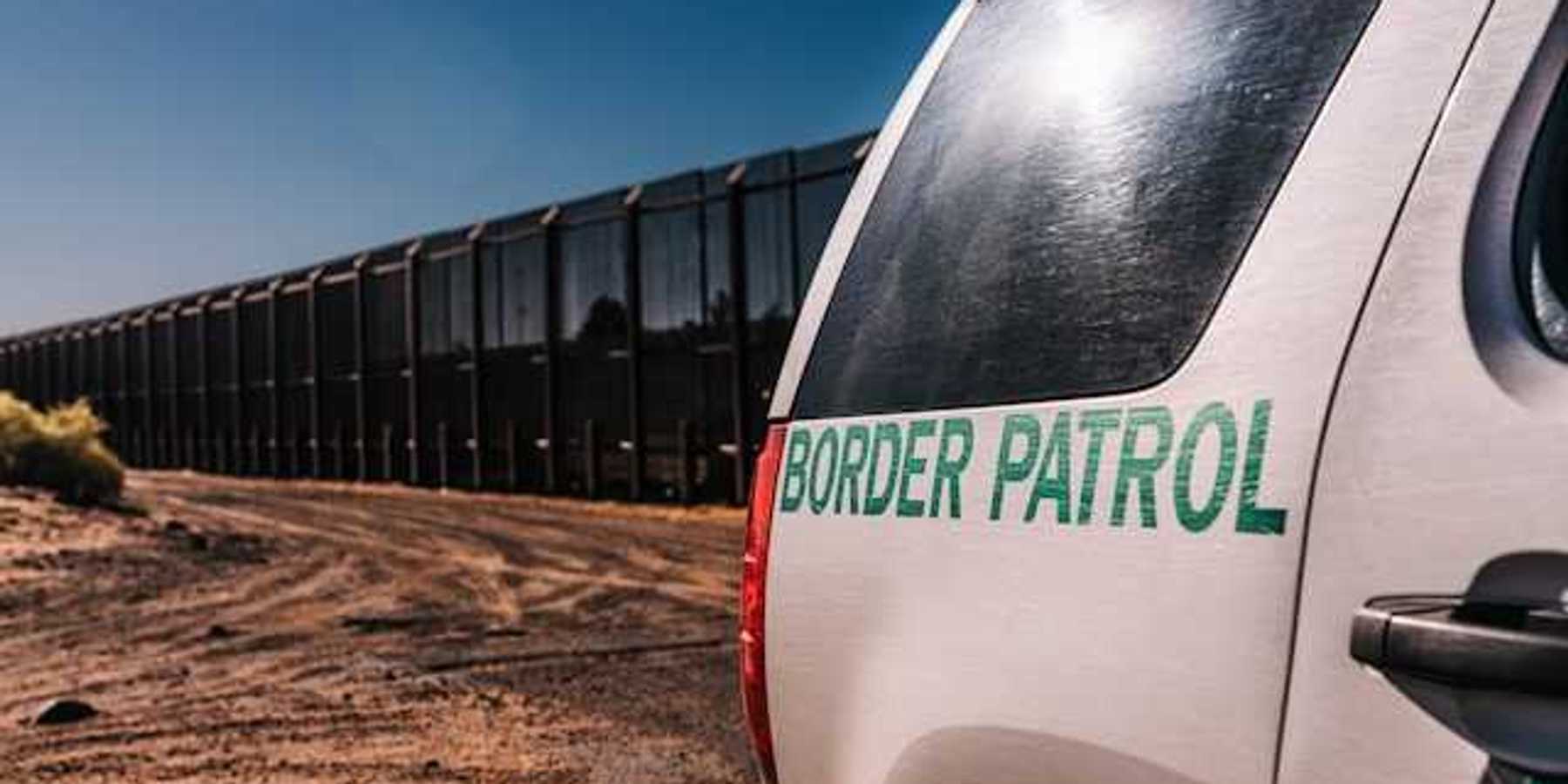 A view of a Border Patrol vehicle next to a tall metal border wall