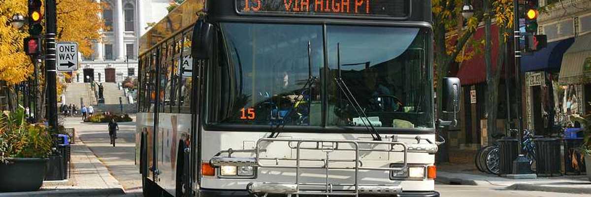 A view of a bus driving down a Madison, WI street with the capitol building in the background