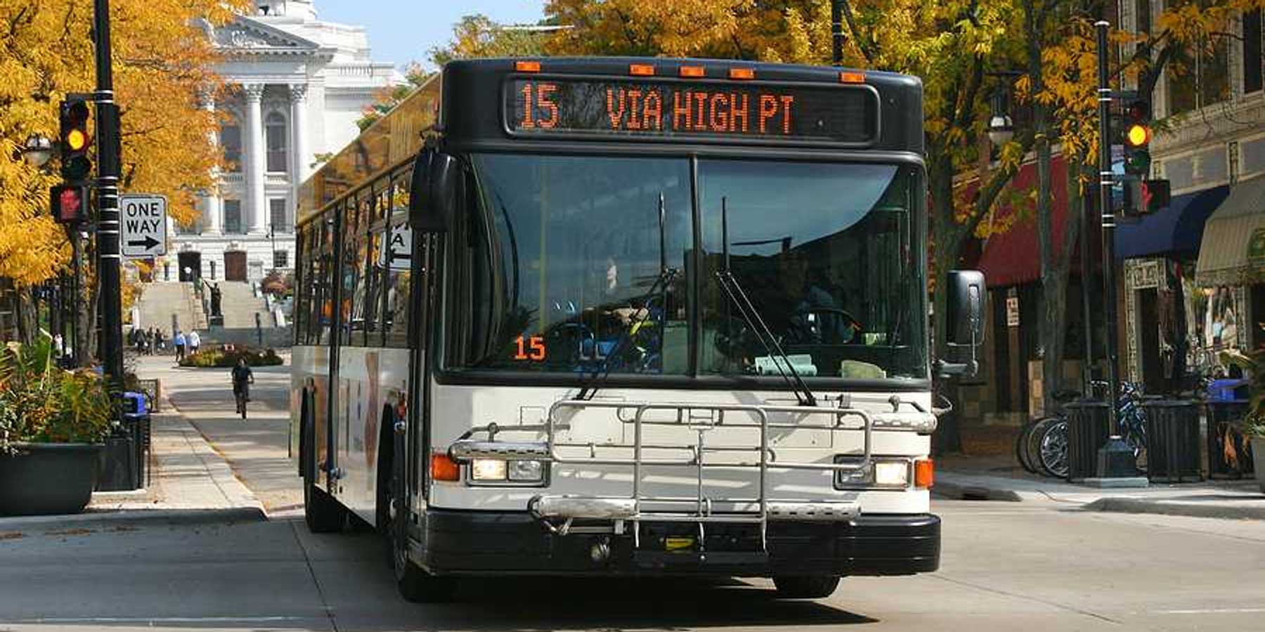 A view of a bus driving down a Madison, WI street with the capitol building in the background