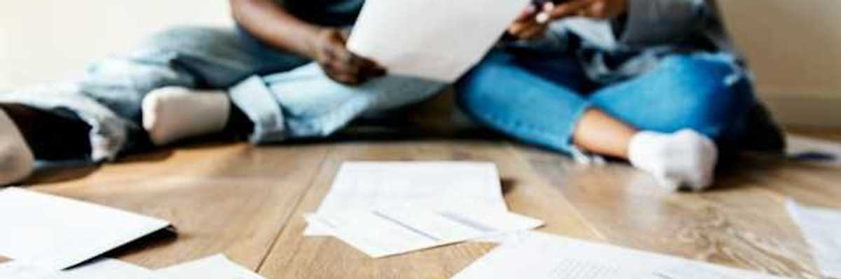 A view of a couple sitting on the floor looking through bills