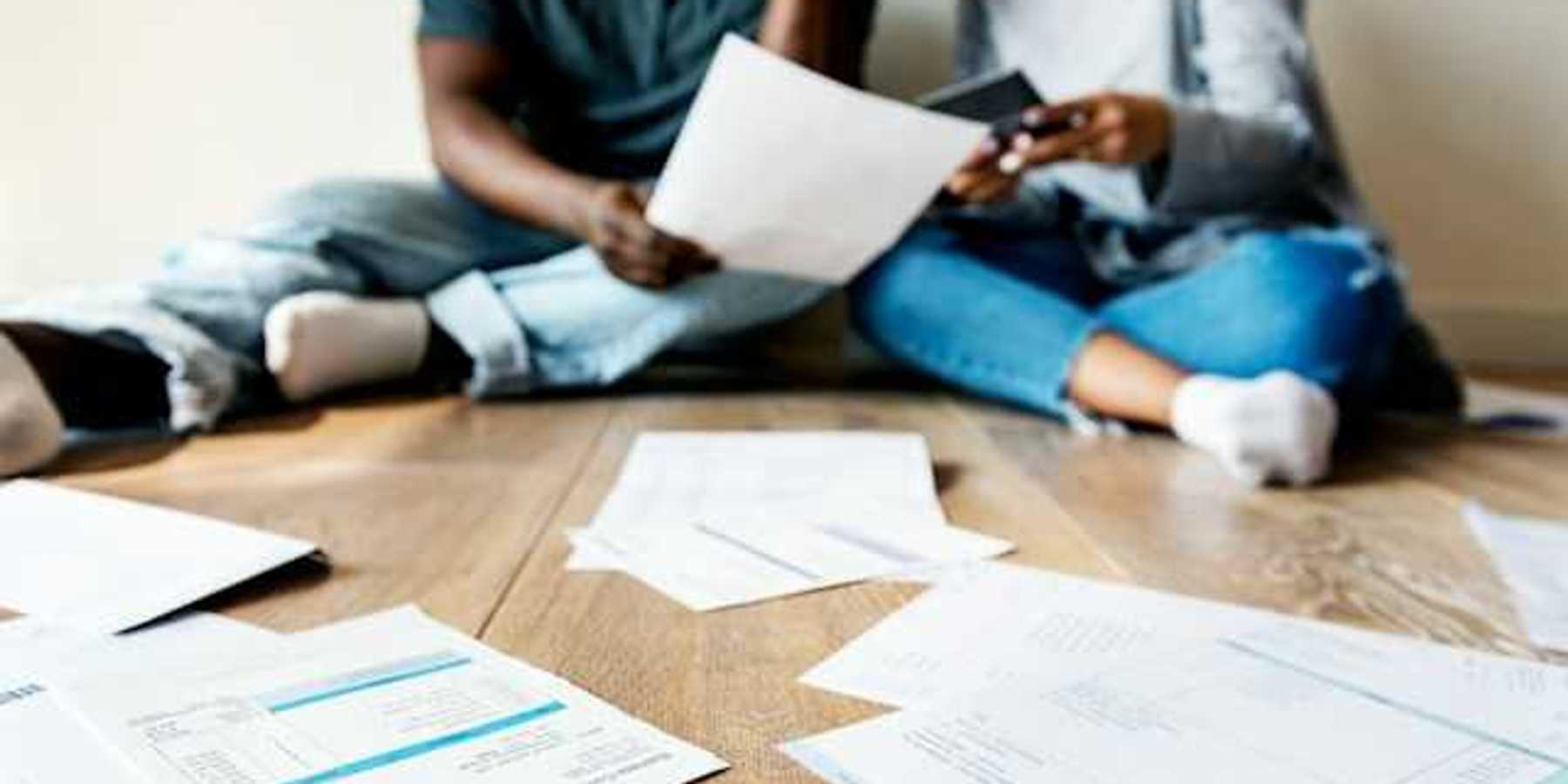 A view of a couple sitting on the floor looking through bills