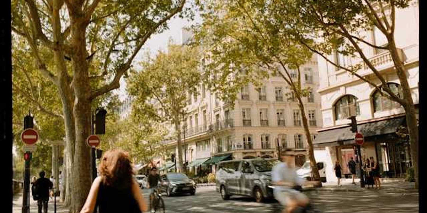 A view of a European street with trees, buildings and people walking and on bikes