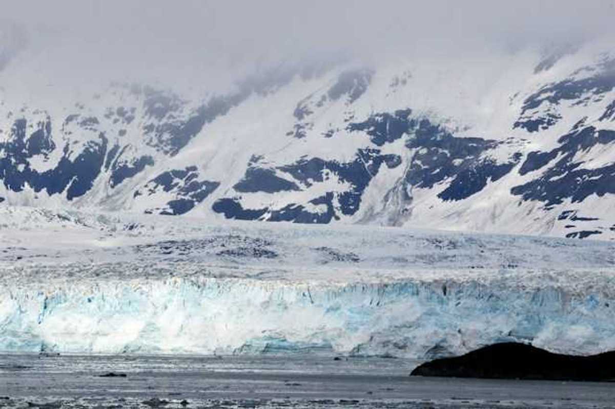 A view of a glacier with snow covered mountains behind it