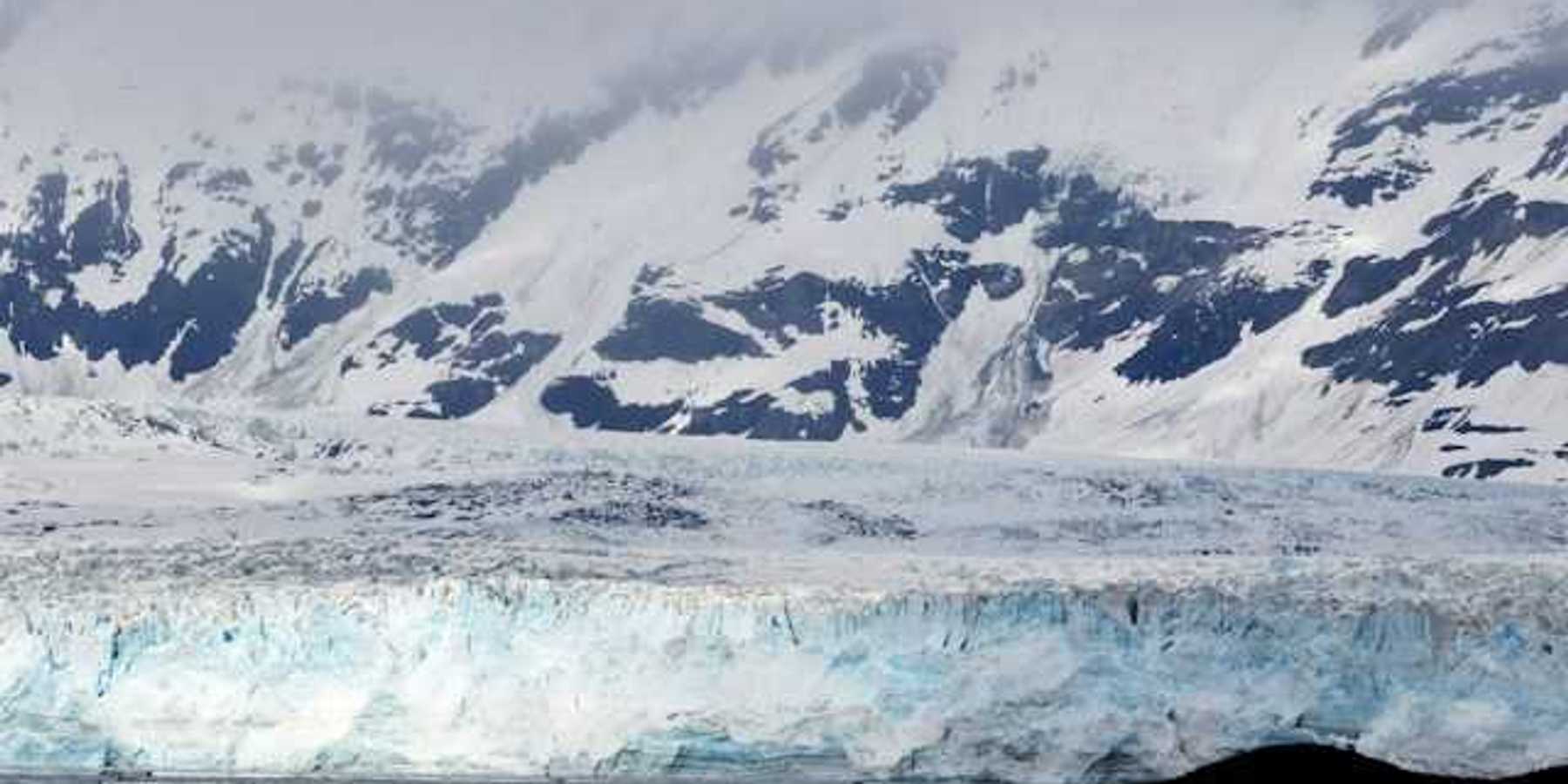 A view of a glacier with snow covered mountains behind it
