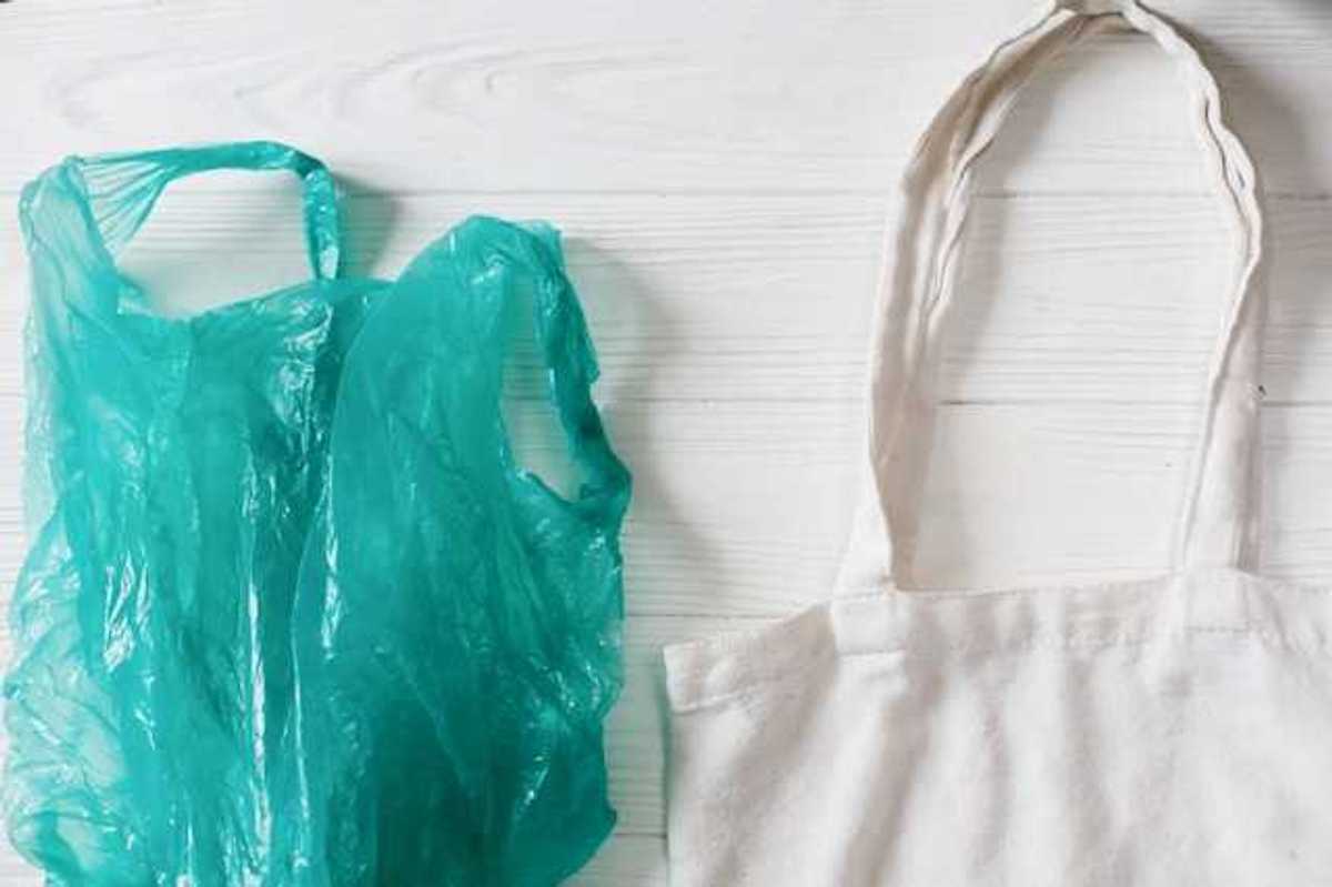 A view of a green plastic bag next to a white reusable bag on a white wooden surface