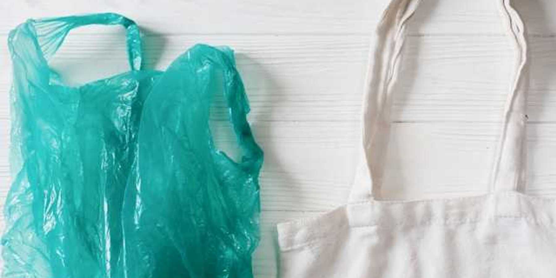 A view of a green plastic bag next to a white reusable bag on a white wooden surface