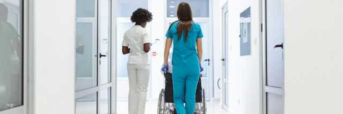 A view of a hospital corridor with two nurses wheeling a patient toward a room