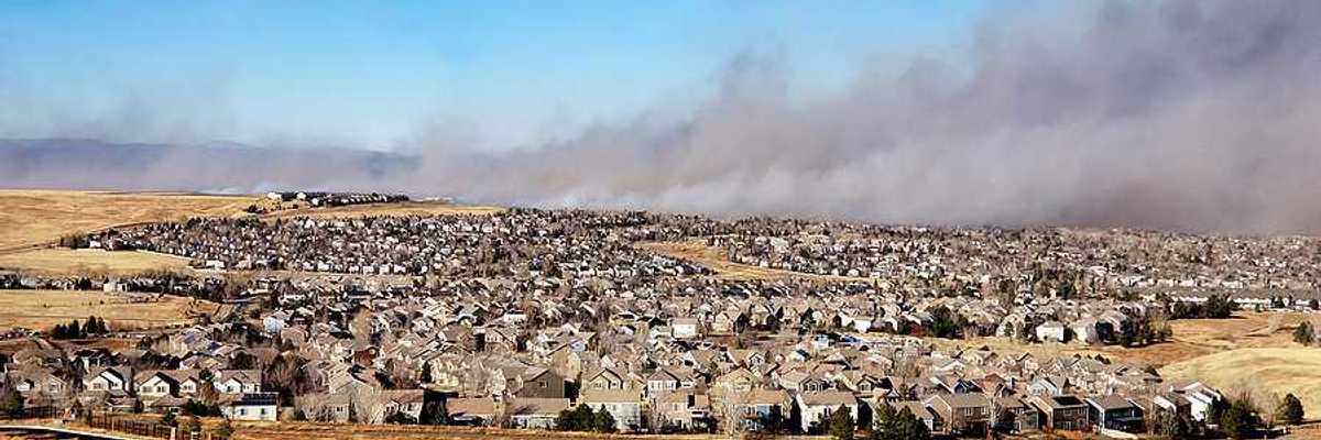 A view of a housing development with a wildfire and smoke in the background