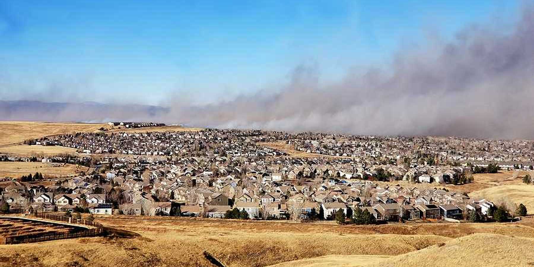A view of a housing development with a wildfire and smoke in the background