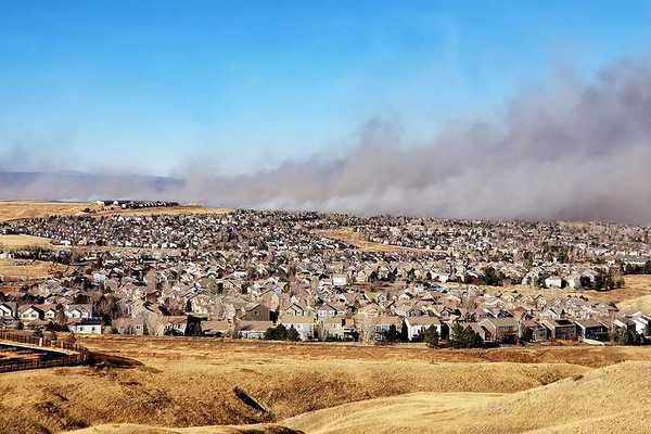 A view of a housing development with a wildfire and smoke in the background