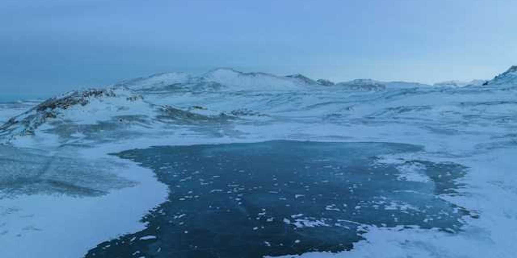 A view of a lake surrounded by ice and snow with mountains in the background