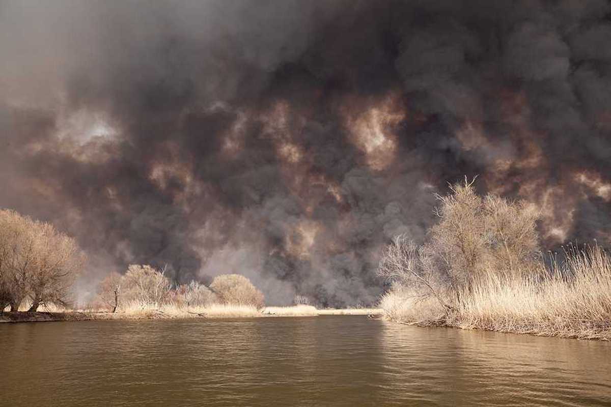 A view of a lake with billowing wildfire smoke in the background