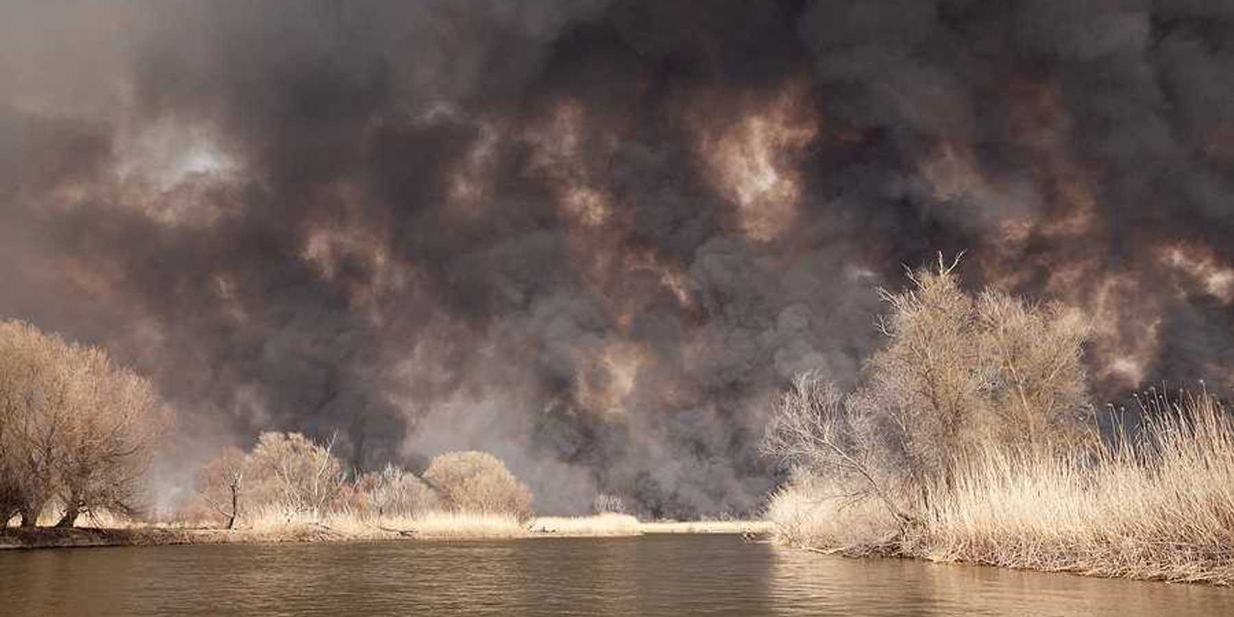 A view of a lake with billowing wildfire smoke in the background