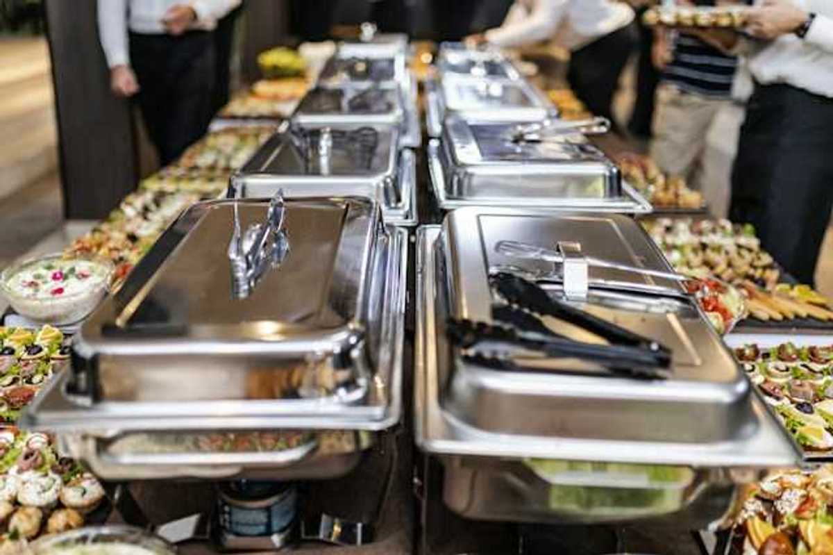 A view of a long buffet table with silver trays and plates of food