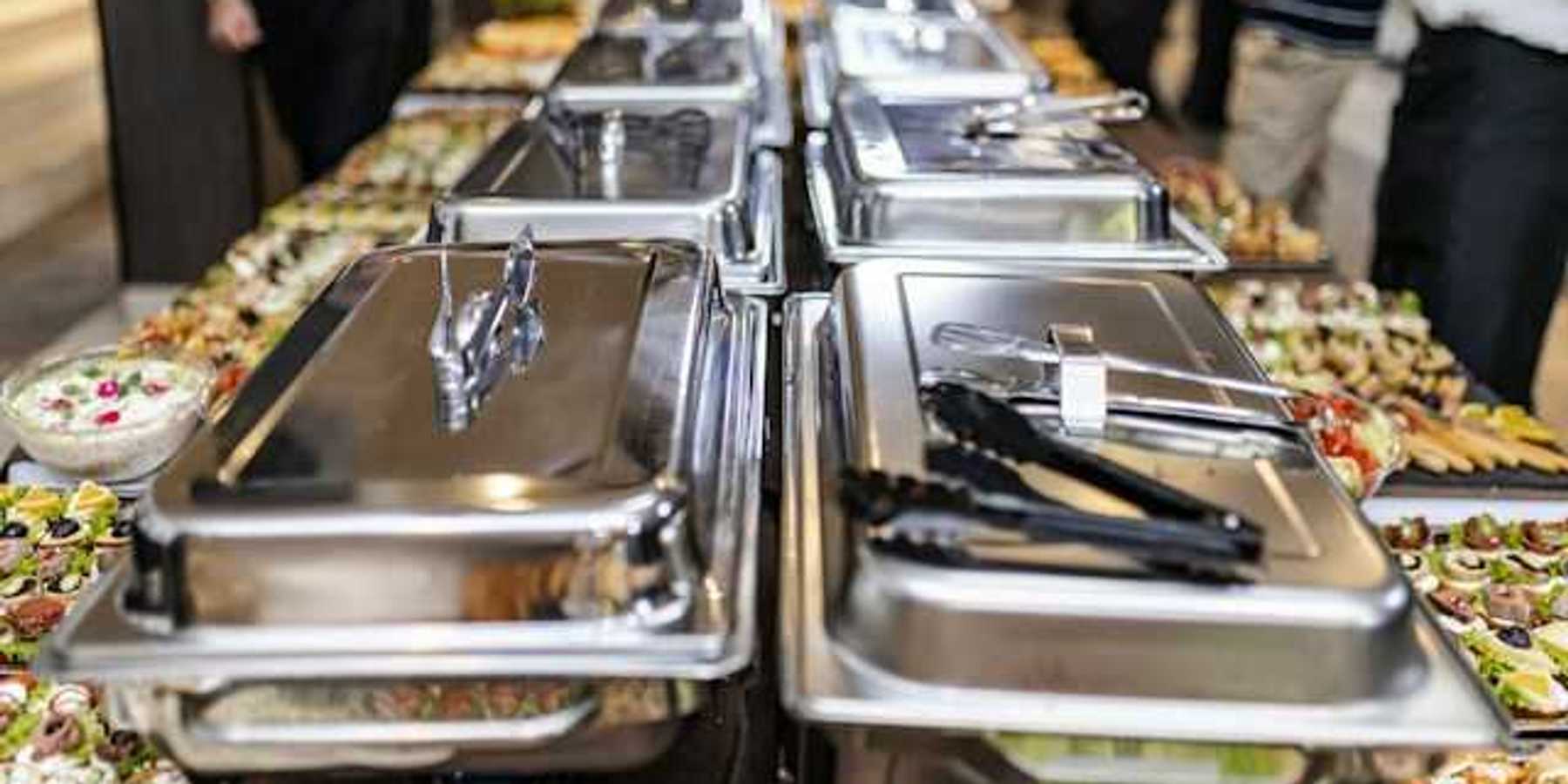A view of a long buffet table with silver trays and plates of food