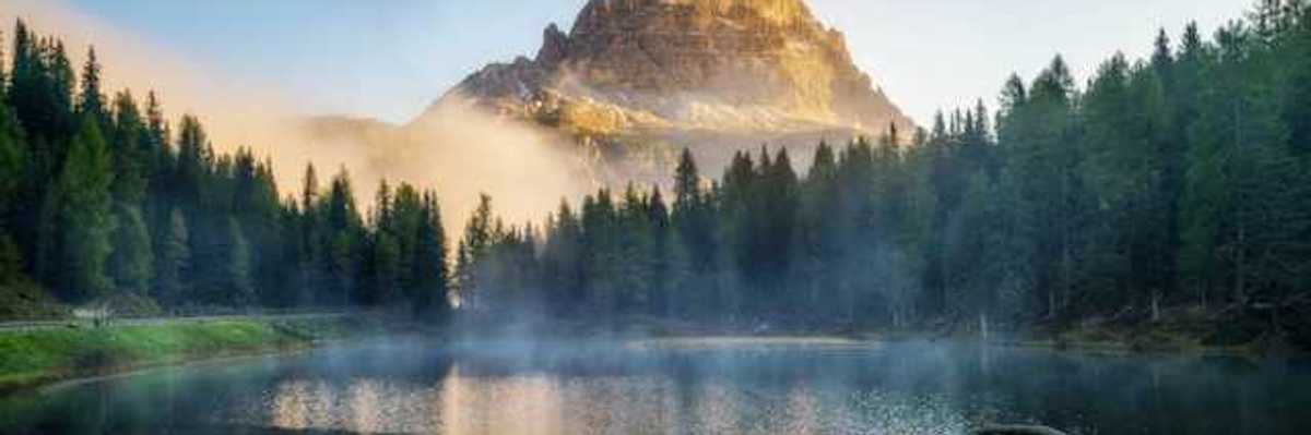 A view of a mountain peak with a small lake and forest trees in the foreground