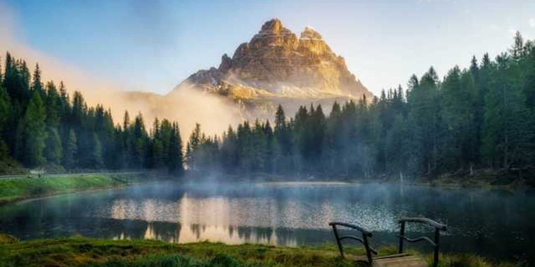 A view of a mountain peak with a small lake and forest trees in the foreground