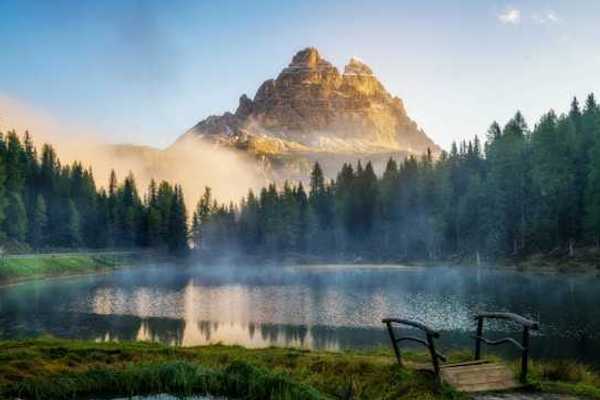 A view of a mountain peak with a small lake and forest trees in the foreground