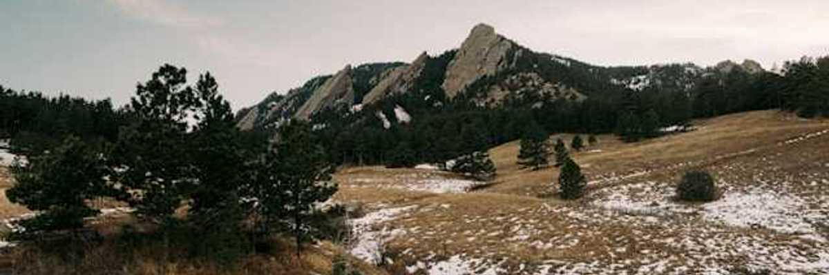 A view of a mountain range with sparse snow in the foreground
