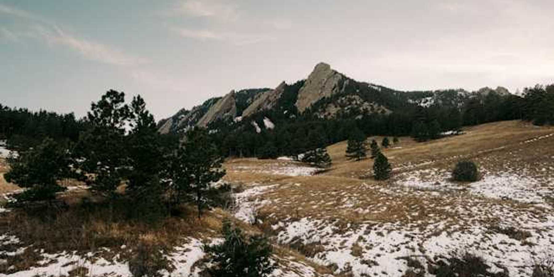 A view of a mountain range with sparse snow in the foreground
