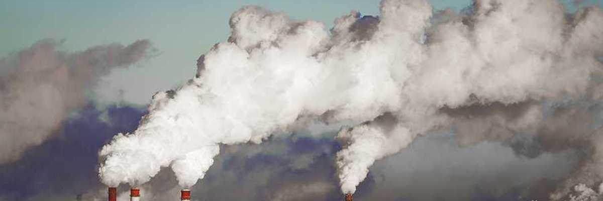 A view of a power plant with red and white smokestacks and pollution billowing into the sky