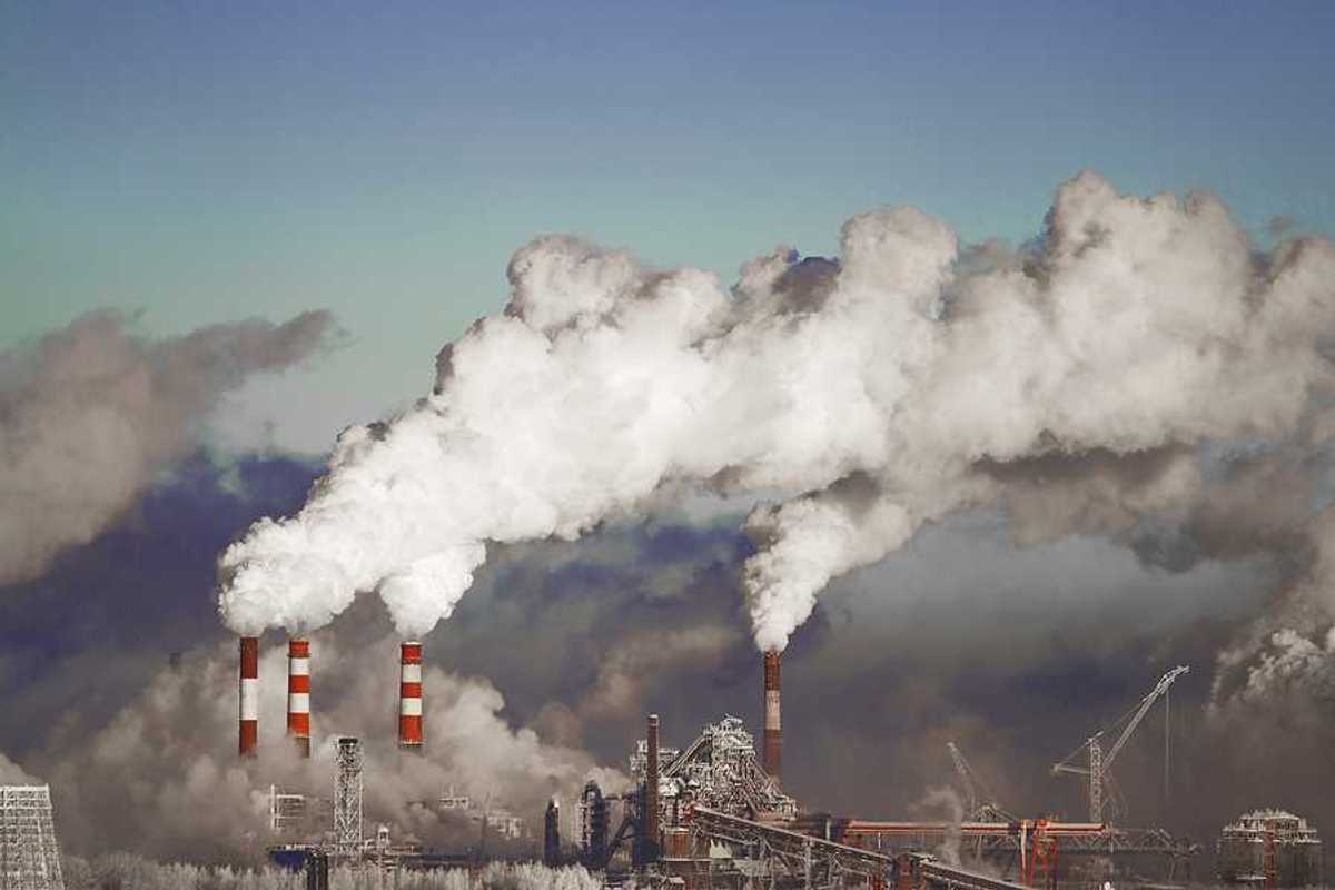 A view of a power plant with red and white smokestacks and pollution billowing into the sky