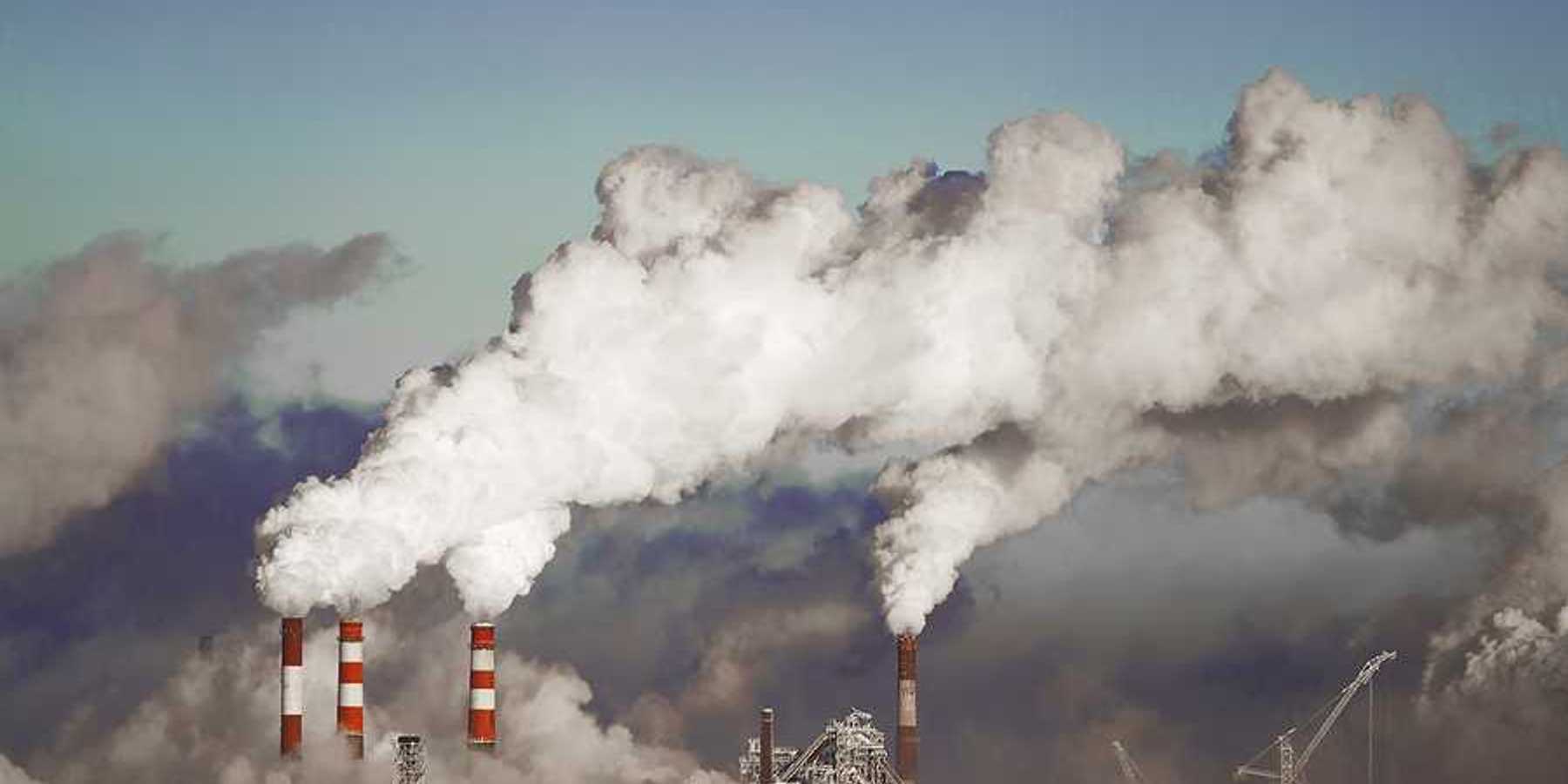 A view of a power plant with red and white smokestacks and pollution billowing into the sky