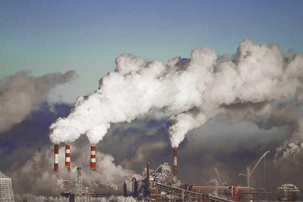 A view of a power plant with red and white smokestacks and pollution billowing into the sky