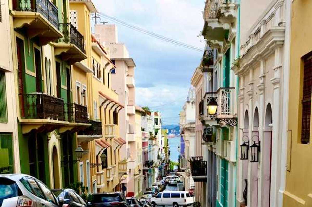 A view of a Puerto Rican street with multicolored buildings and cars and the ocean in the far distance