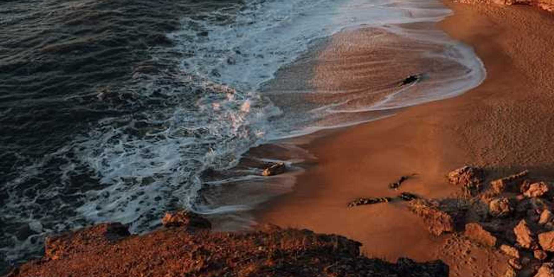 A view of a rocky beach from above with waves crashing on the shore