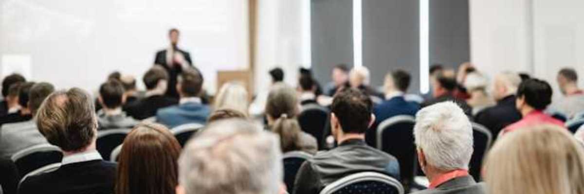 A view of a speaker at a conference from the back of the room