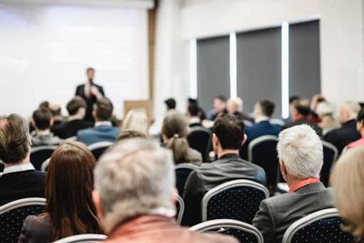 A view of a speaker at a conference from the back of the room