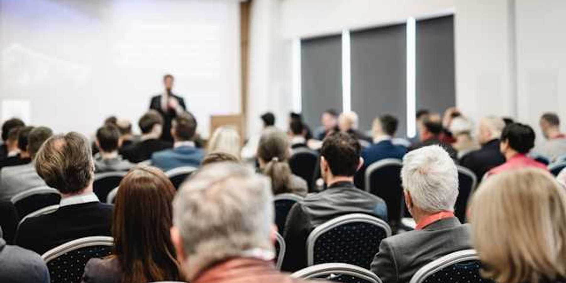 A view of a speaker at a conference from the back of the room