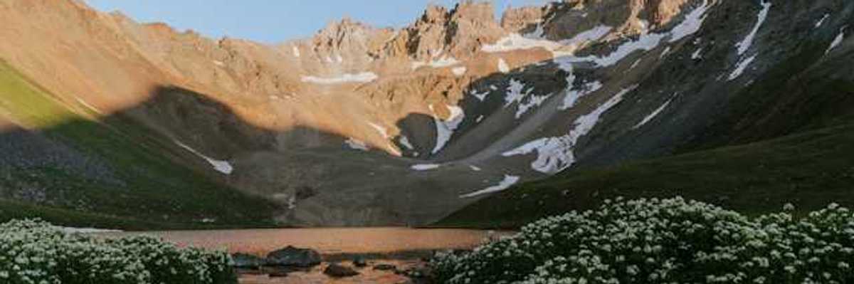 A view of a valley with mountains in the background with melting snow on their banks