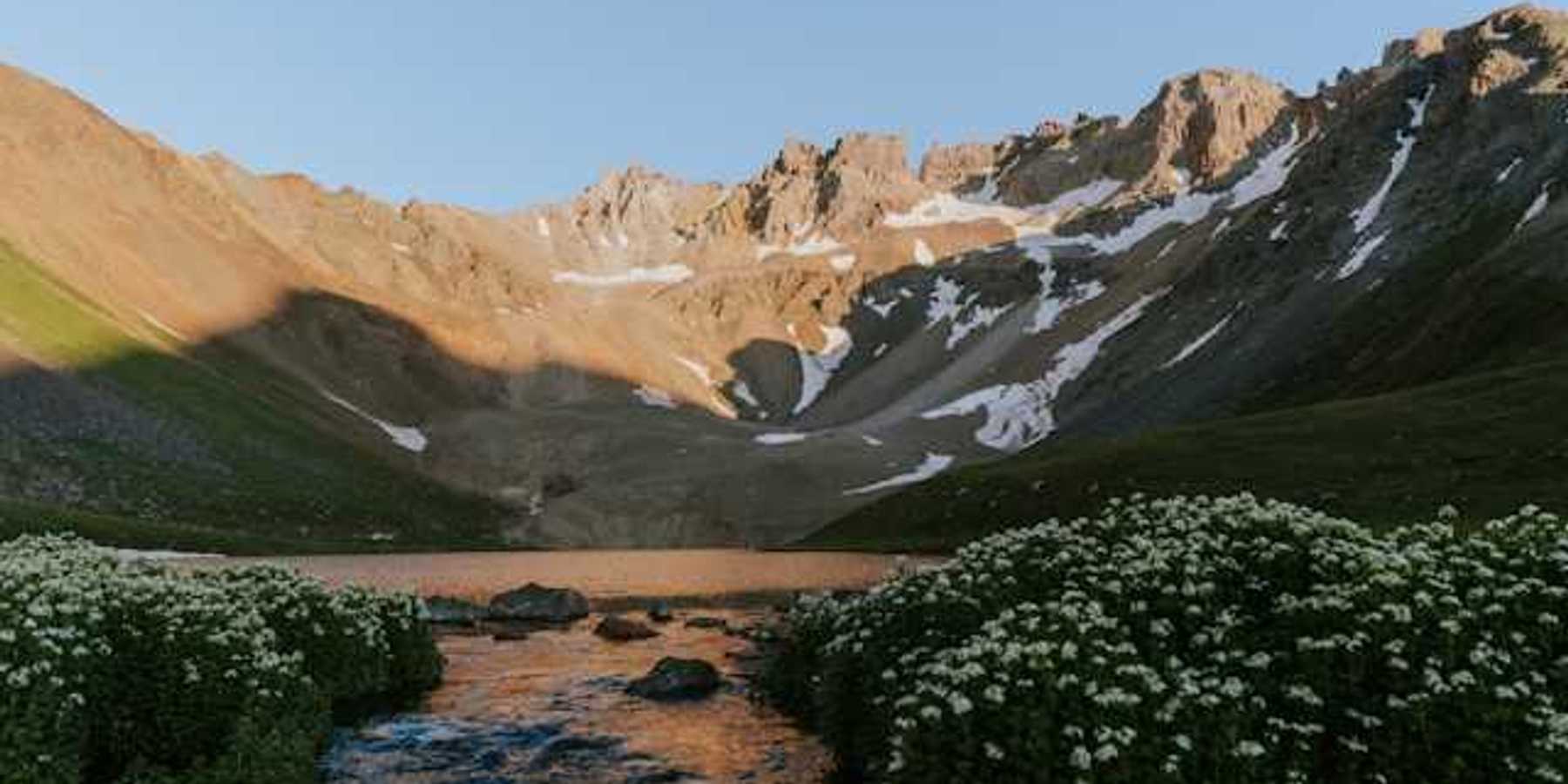 A view of a valley with mountains in the background with melting snow on their banks