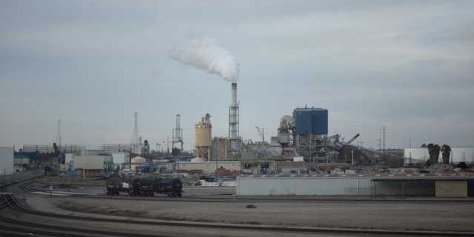 A view of an industrial factory with smoke rising out of a smokestack