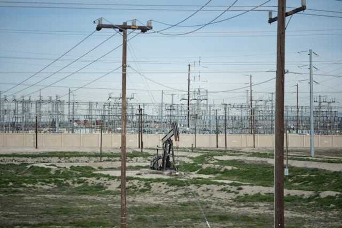 A view of energy lines with a small oil pump jack in a sandy field