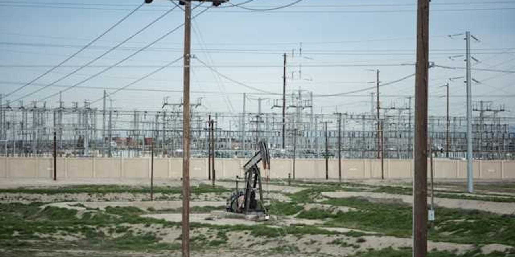 A view of energy lines with a small oil pump jack in a sandy field