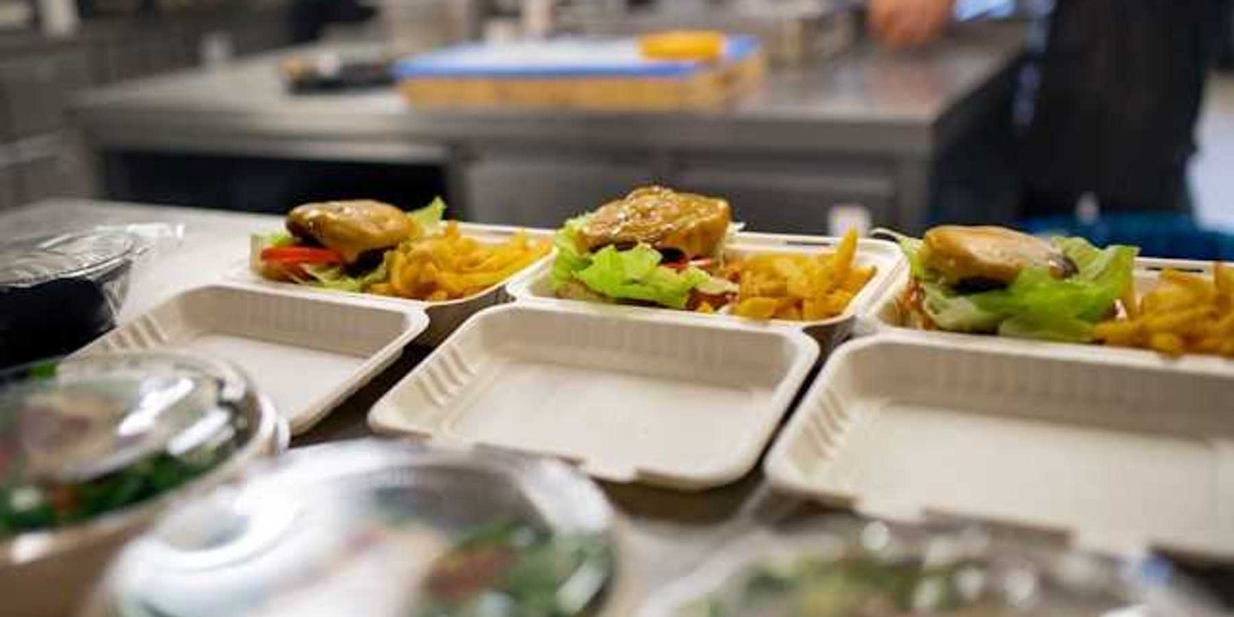 A view of food containers in a kitchen filled with burgers, fries and salad