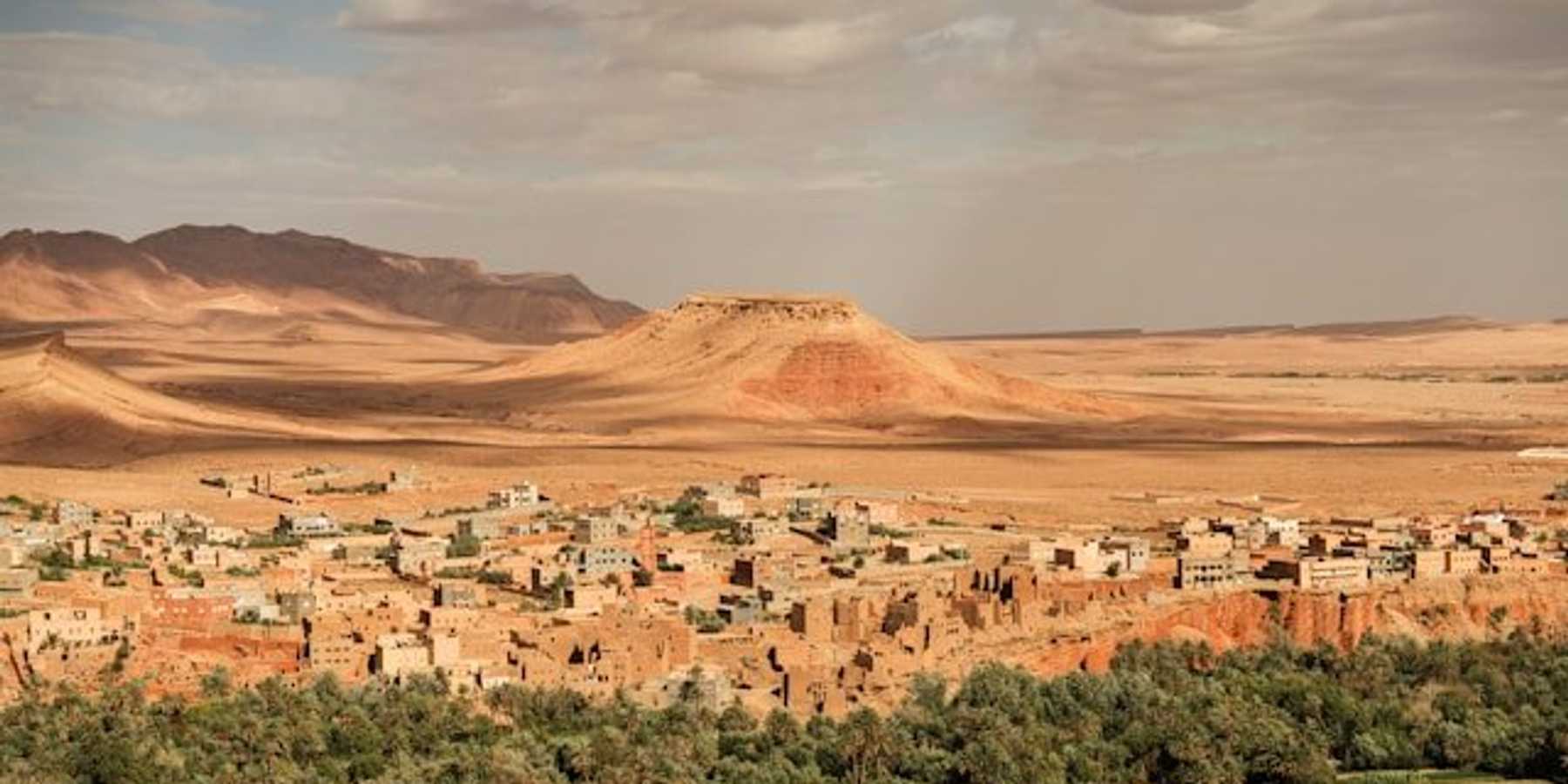 A view of green fields with desert and a small village in the background.